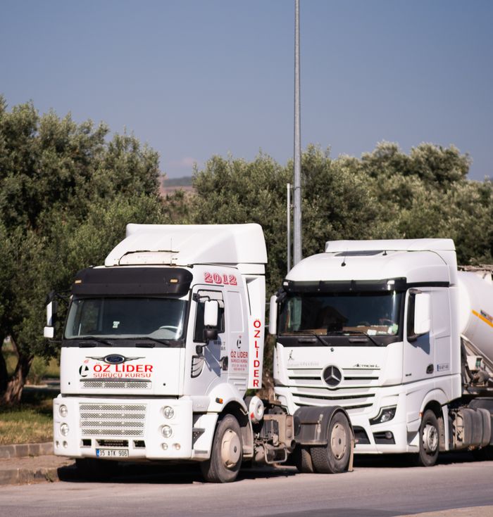 Two commercial trucks parked on a sunny day in İzmir, Türkiye, among greenery.